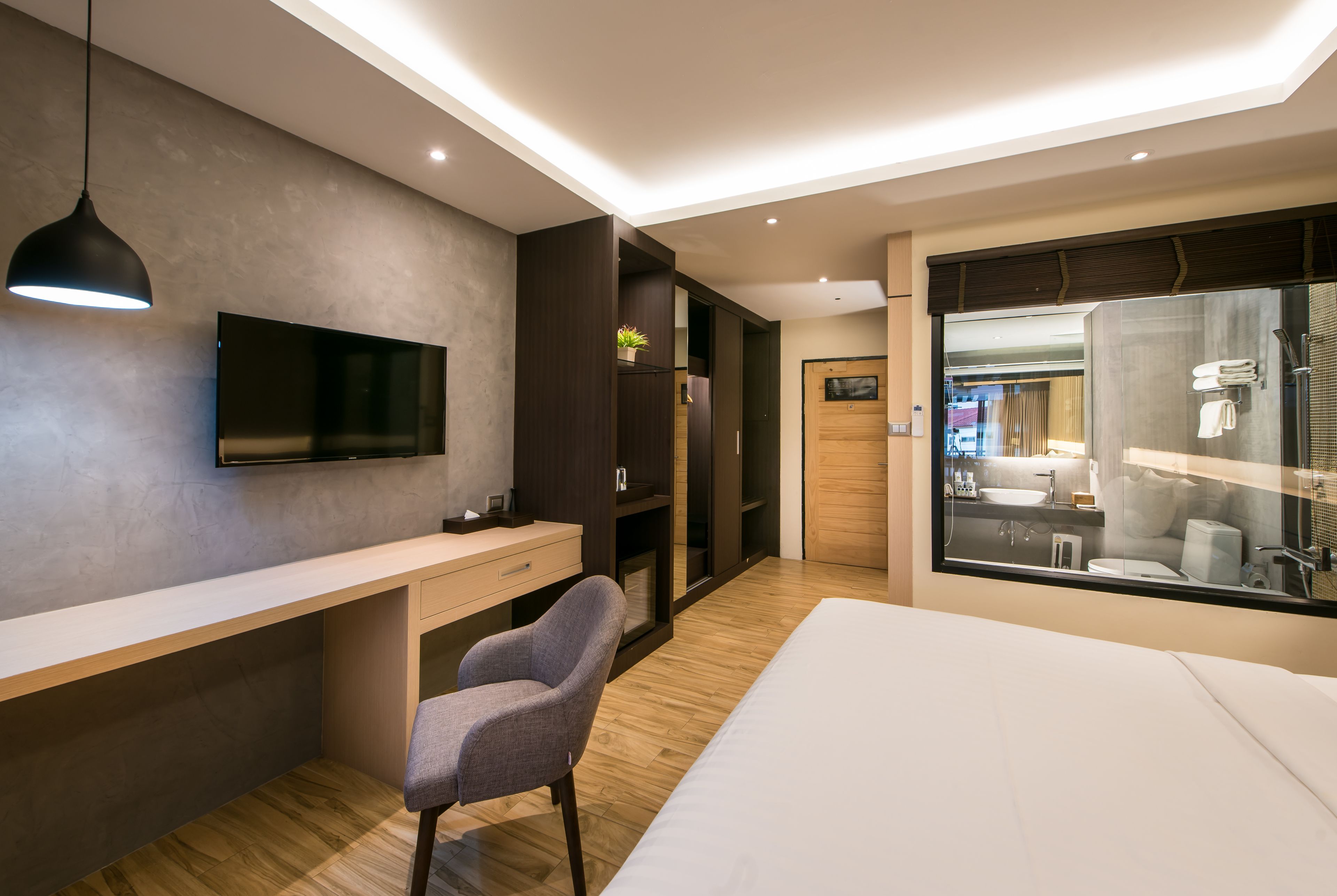 Habitación de hotel moderna con una cama grande, un escritorio con silla, televisor y baño con cabina de ducha de vidrio.