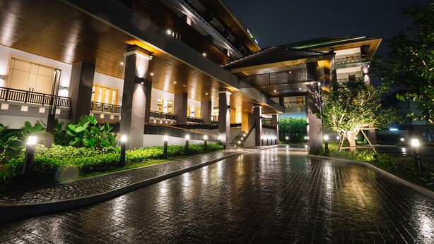 A modern hotel with a spacious outdoor area featuring a wet pavement, well-lit balconies, and a central staircase. - Nadee 10 Resort & Hotel (Khon Kaen)