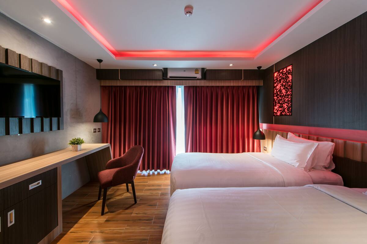A hotel room with a desk, two beds, a TV, and a red-lit ceiling.