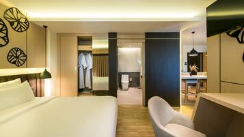 A hotel room with a large bed, a desk, a chair, a wardrobe, and a bathroom visible through an open door.