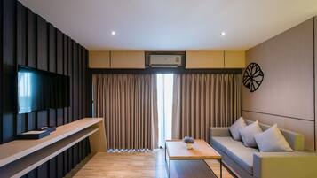 Una sala de estar moderna con una televisión de pantalla plana, un sofá, una mesa de centro y un gran ventanal con cortinas.