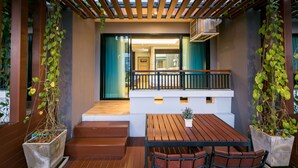 A covered outdoor seating area with a wooden table and chairs, a small potted plant, and a staircase leading to an entrance. - Nadee 10 Resort & Hotel (Khon Kaen)