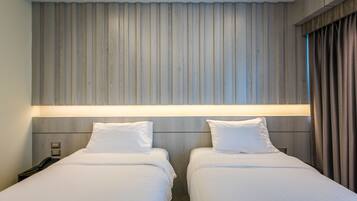 A hotel room with two beds, a wooden headboard, a bedside table with a phone, and a window with curtains.