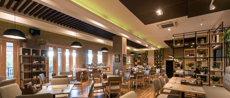 Un restaurante espacioso con varias zonas de comedor, mobiliario de madera y estanterías con plantas.