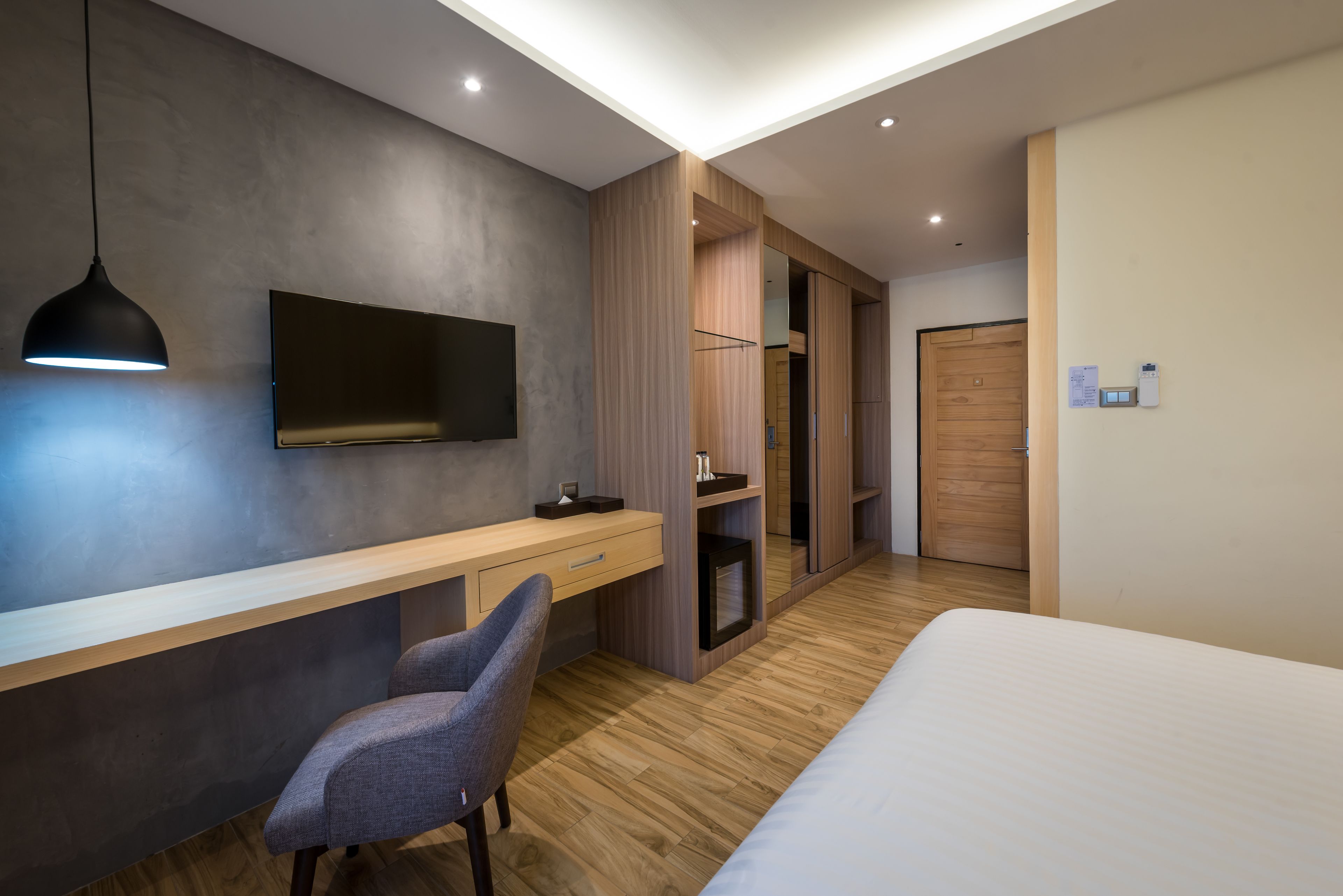 Une chambre moderne avec un plancher en bois, un lit, un bureau avec une chaise, un téléviseur fixé au mur et une armoire.