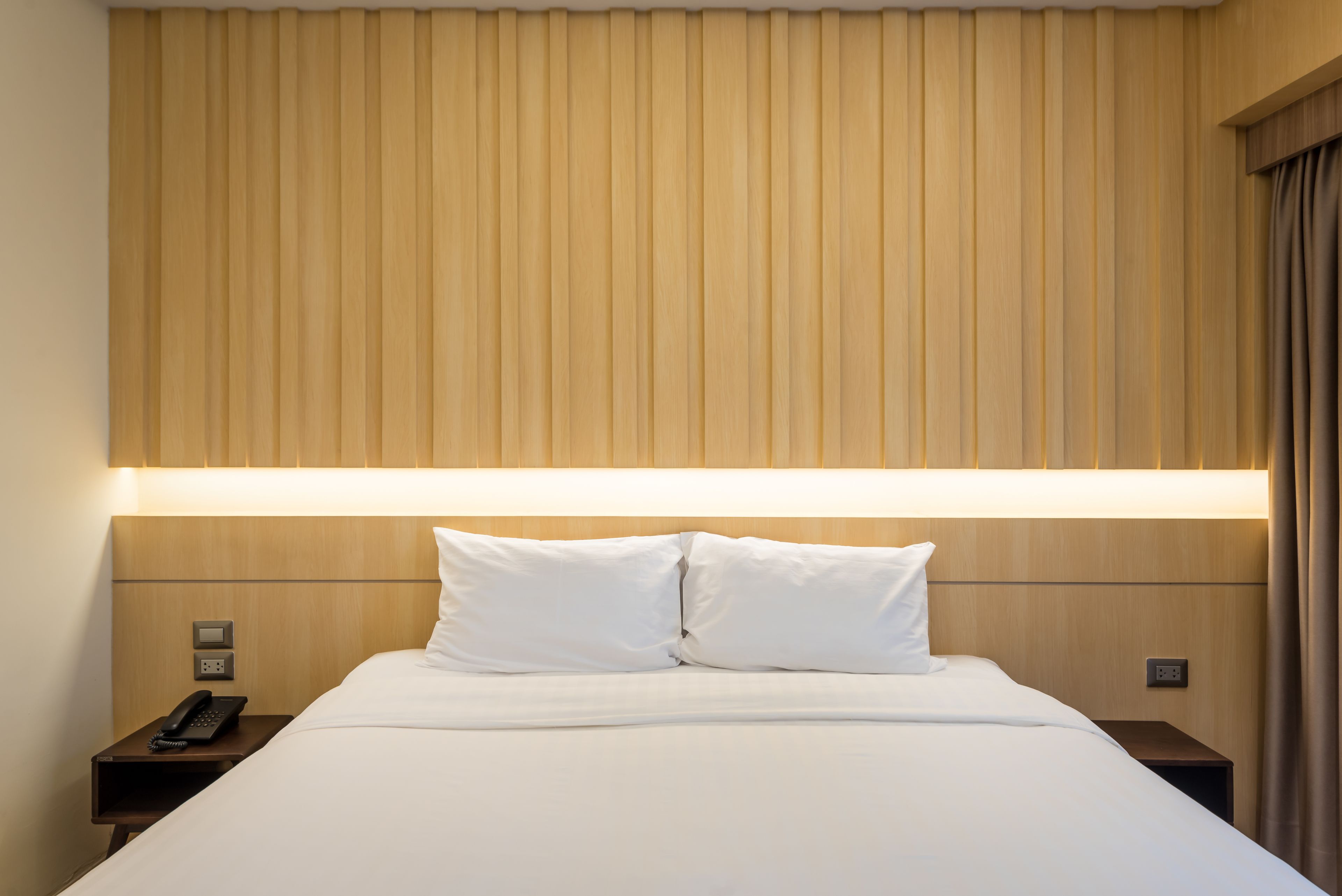 Una habitación de hotel con una cama grande, una mesita de noche con teléfono y una lámpara fijada a la pared.