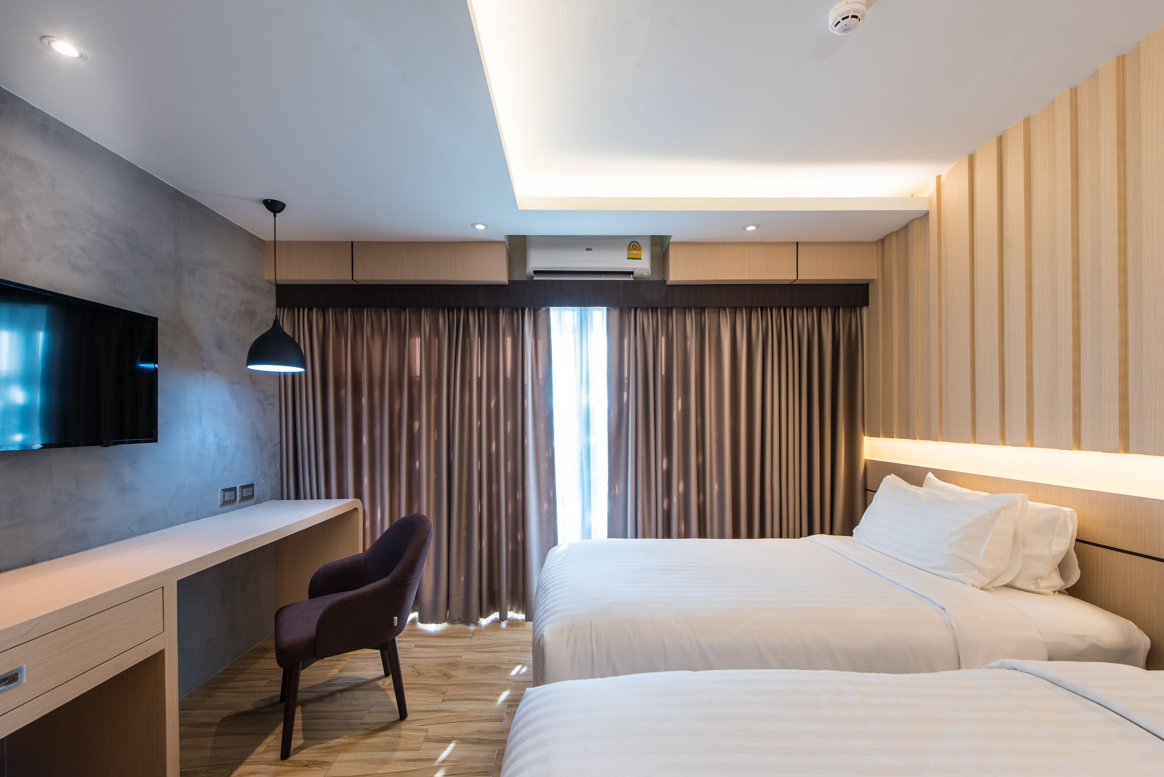Une chambre d’hôtel équipée d’un bureau, de deux lits, d’une télévision et d’une grande fenêtre avec des rideaux.
