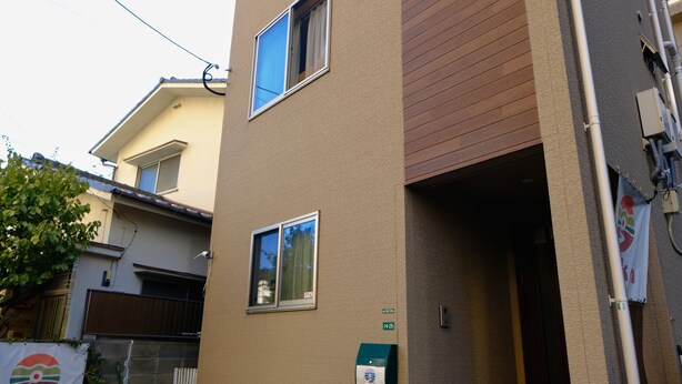 A modern two-story building with a beige facade, a small outdoor seating area, and a visible entrance. - Fukuoka Guest House Jikka (Fukuoka)