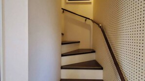 A staircase with a handrail, a wall-mounted picture, and a perforated wall design. - Fukuoka Guest House Jikka (Fukuoka)