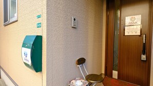 A hotel entrance with a wooden door, a green mailbox, and a chair outside. - Fukuoka Guest House Jikka (Fukuoka)