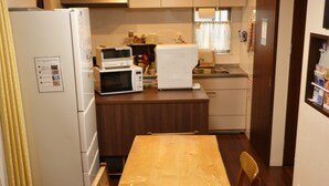 A compact kitchen with a wooden dining table, built-in microwave, and white refrigerator. - Fukuoka Guest House Jikka (Fukuoka)