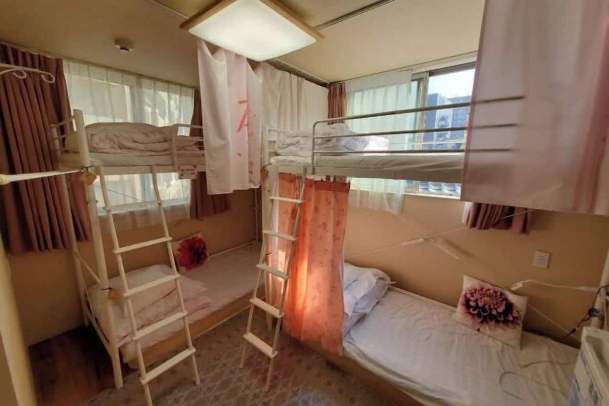 A bunk bed room with a ladder, a small table, and a window with curtains.