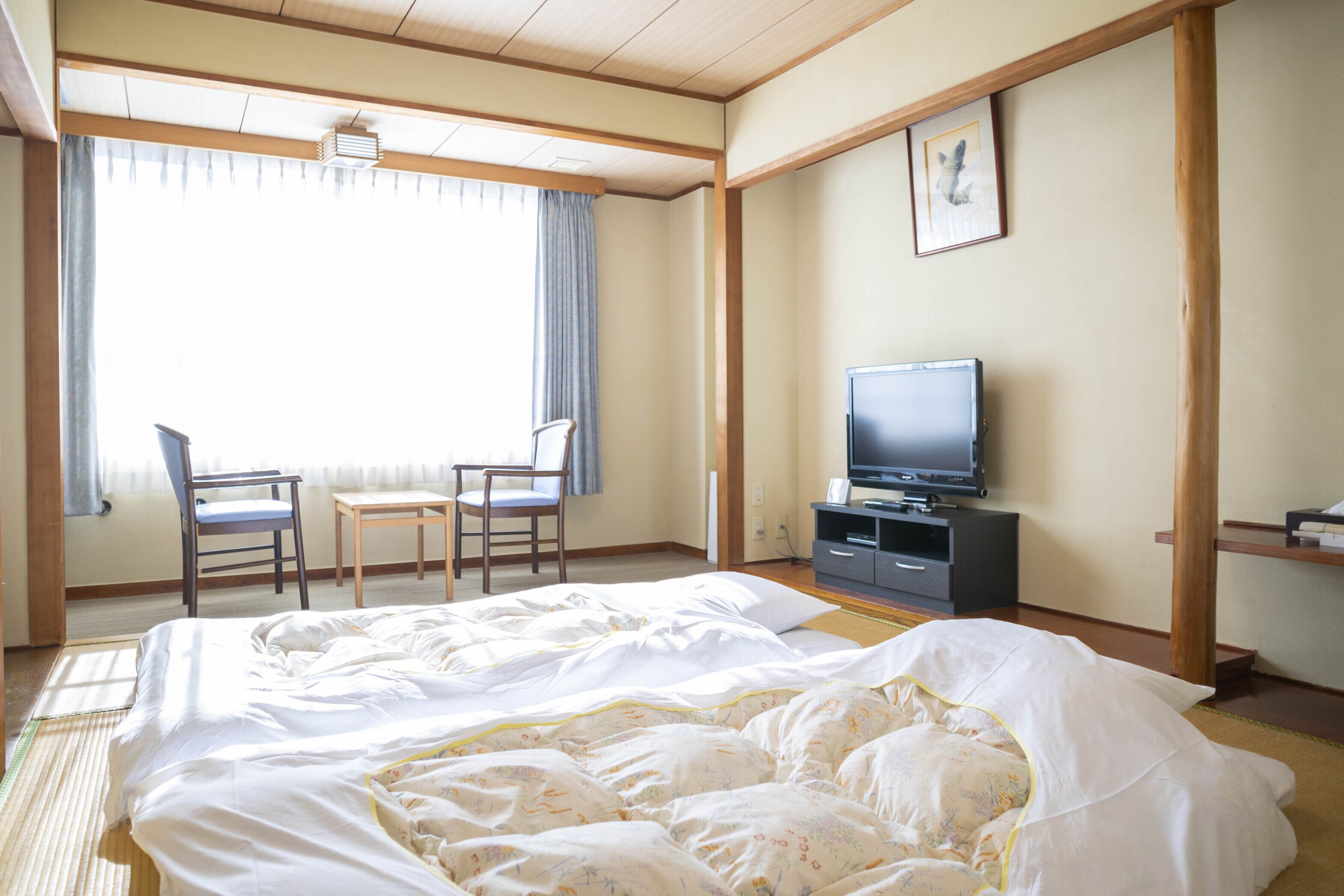 A hotel room with a bed, two chairs, a TV, and a picture on the wall.