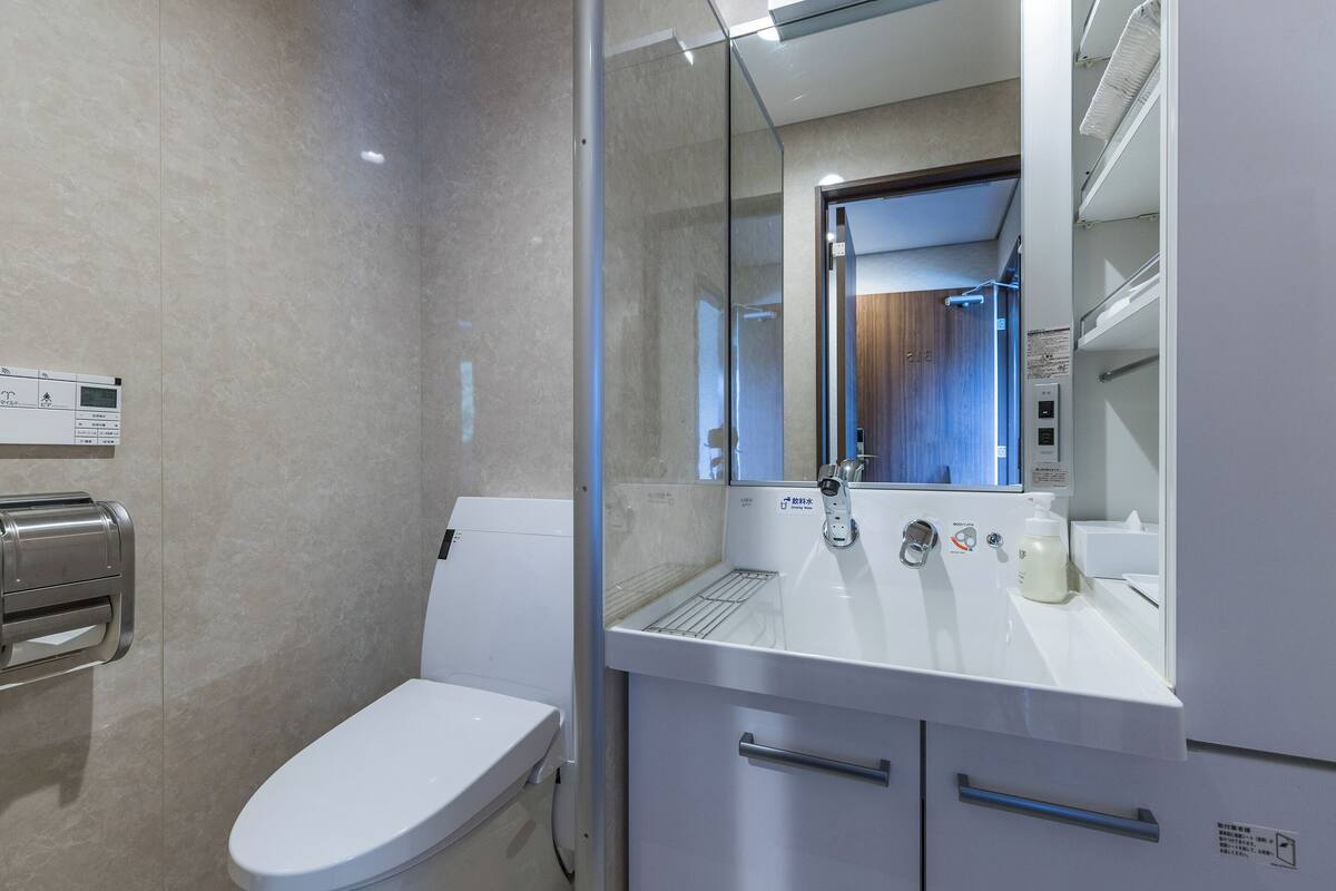 A modern bathroom with a toilet, a glass shower enclosure, a sink with a mirror, and a hand dryer.