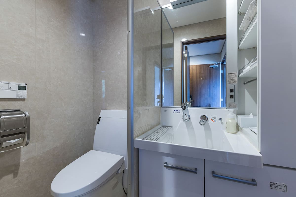 Un baño moderno con inodoro, cabina de ducha de vidrio, lavabo con espejo y secamanos.