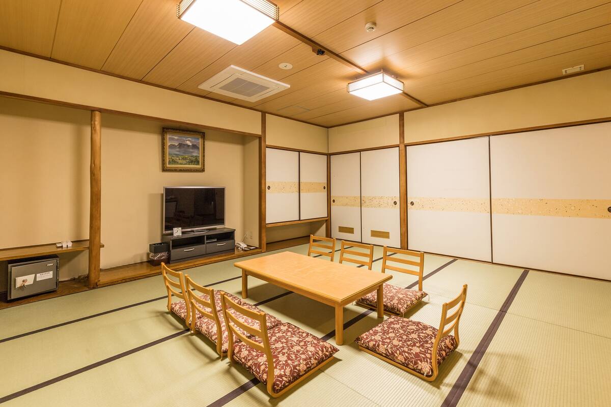 A tatami mat room with a wooden table and chairs, a television, and sliding doors.