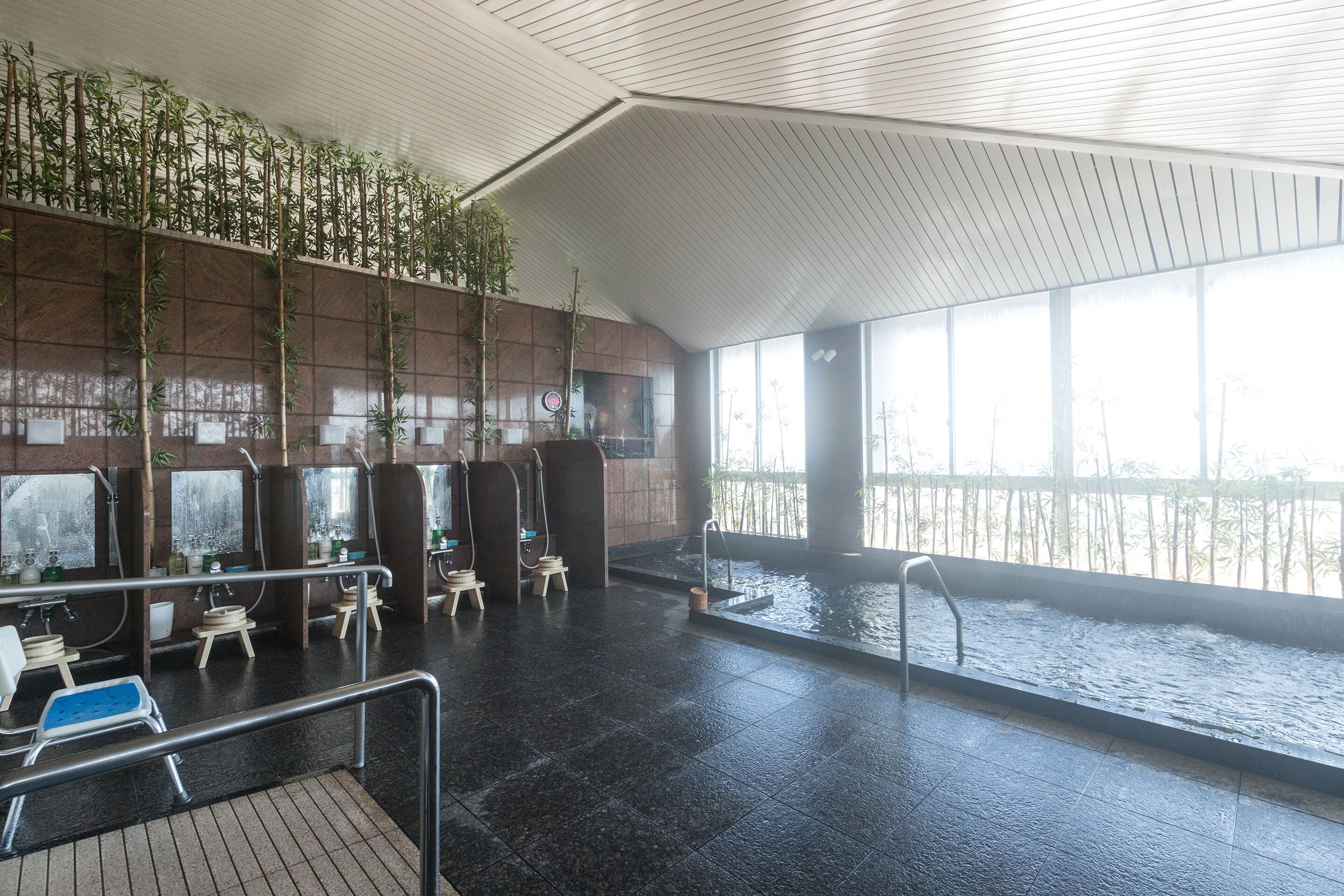 A modern indoor pool area with multiple water features, seating areas, and a large window providing natural light.