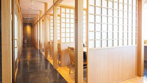 Un couloir doté de portes coulissantes en bois, d’un sol carrelé et d’un espace détente avec des chaises et une table.
