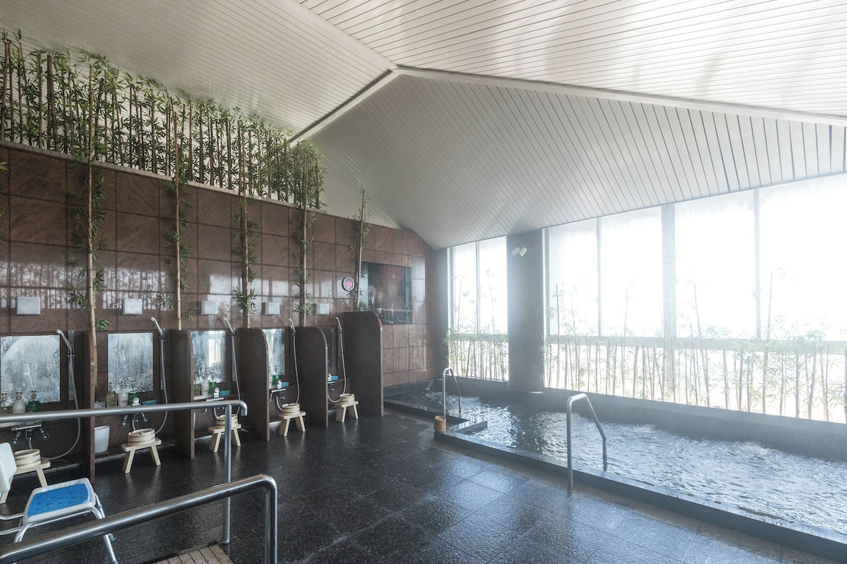 An indoor swimming pool with multiple shower areas, a tiled floor, and a view of the water outside.