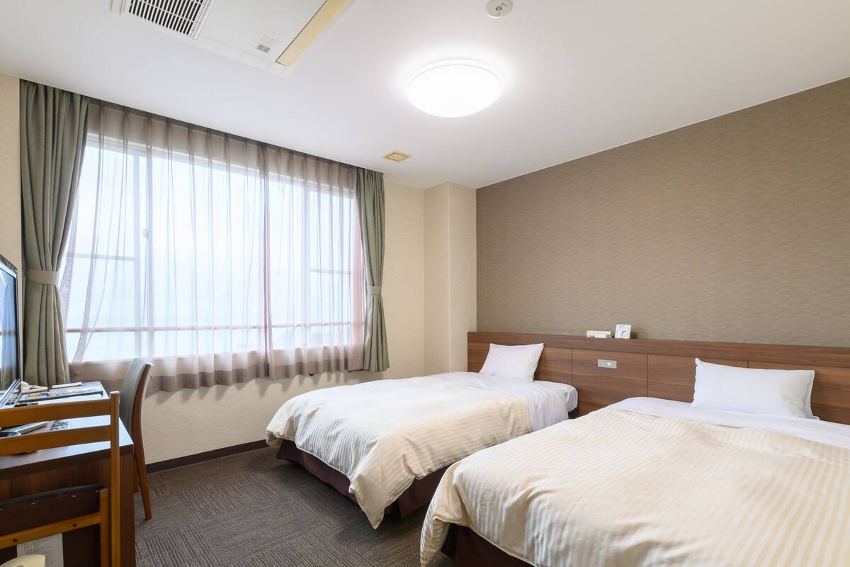 A hotel room with two beds, a desk, and a chair.