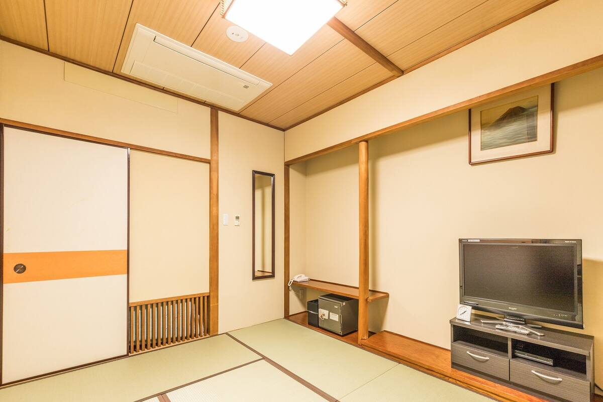 A traditional Japanese room with tatami flooring, a sliding door, a television, and a small shelf with a telephone.