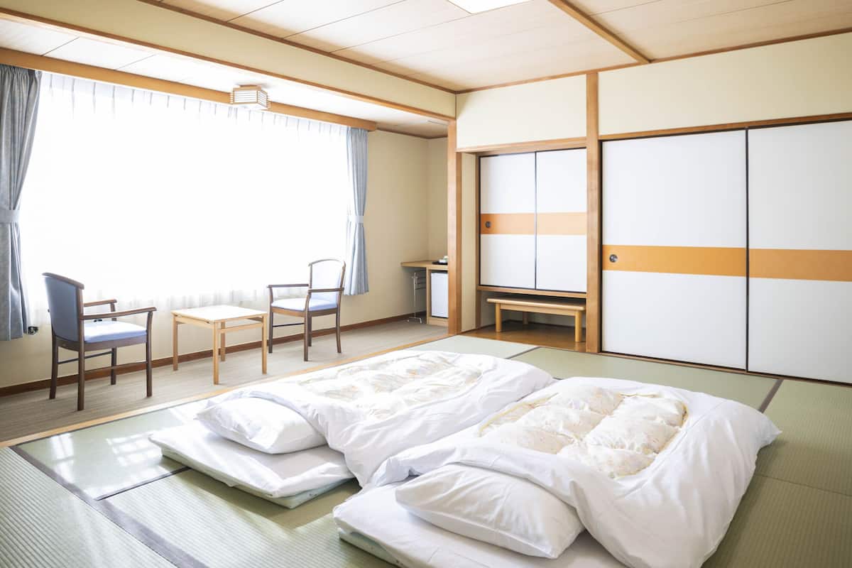 Une chambre d’hôtel avec des tatamis, un lit, un bureau, une chaise et une armoire.