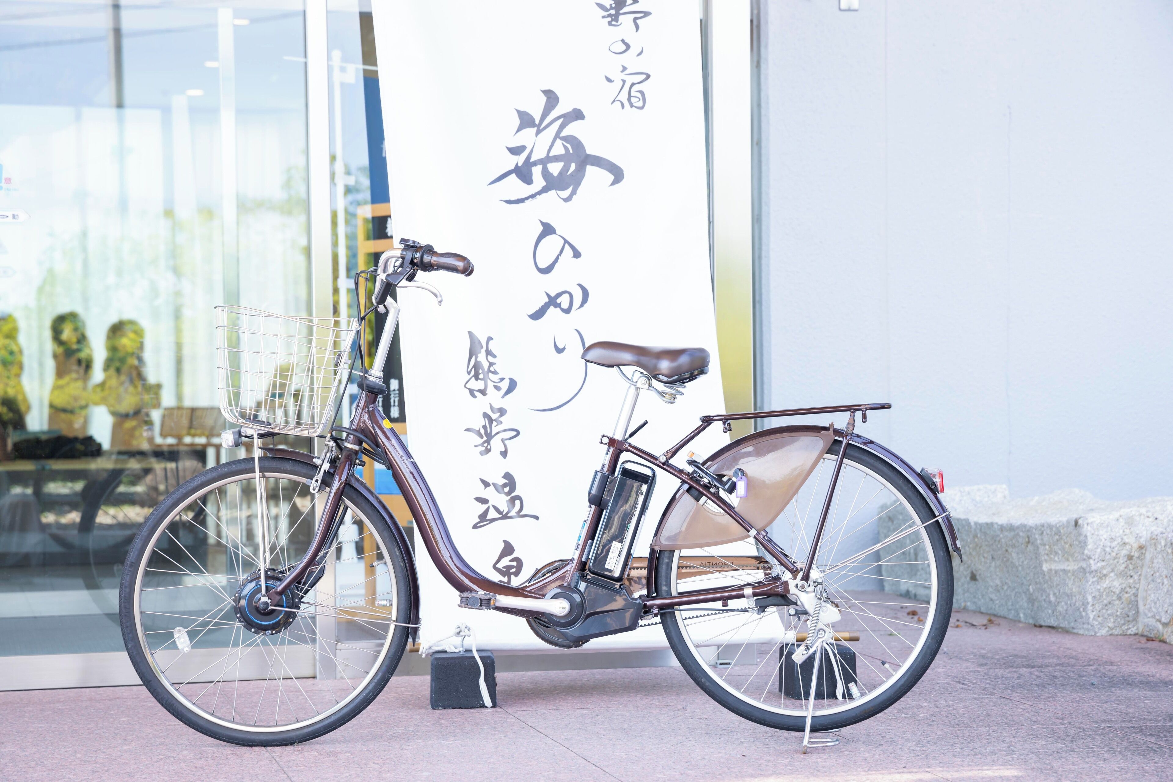 A stationary bicycle with a basket and a seat, parked in front of a building with a large vertical sign with Japanese characters.