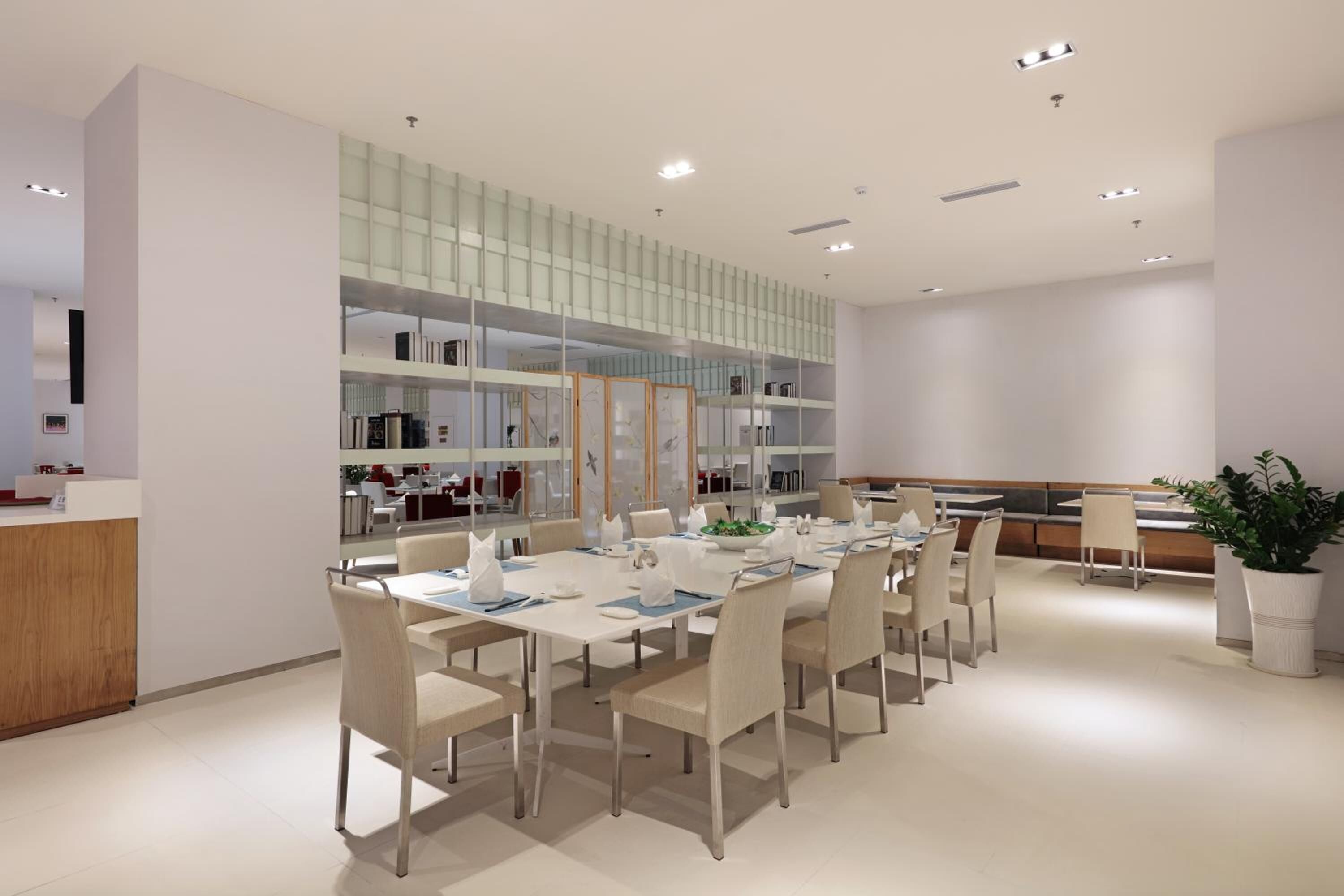 A modern dining area with a long table, chairs, and a potted plant.