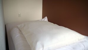 Een bed met witte beddengoed in een kamer met een effen muur en een bruine accentmuur.