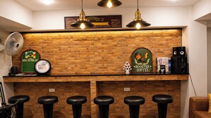 A bar area with a brick wall, five stools, a fan, and a sign that reads 'ROOSTER GOOSE COFFEE.' - 101 Seoul Hostel (Bangkok)