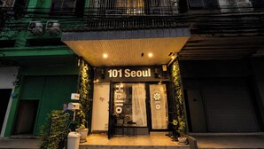 A building with a sign reading '101 Seoul' at the entrance, a small outdoor seating area, and potted plants. - 101 Seoul Hostel (Bangkok)
