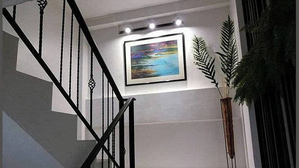 A staircase with black railings, a framed painting on the wall, and a tall plant beside it. - 101 Seoul Hostel (Bangkok)