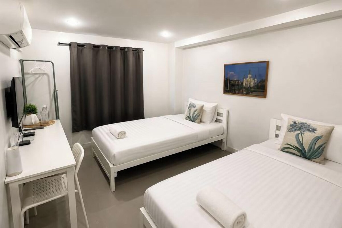 A hotel room with two beds, a desk, a chair, a TV, and a painting on the wall.