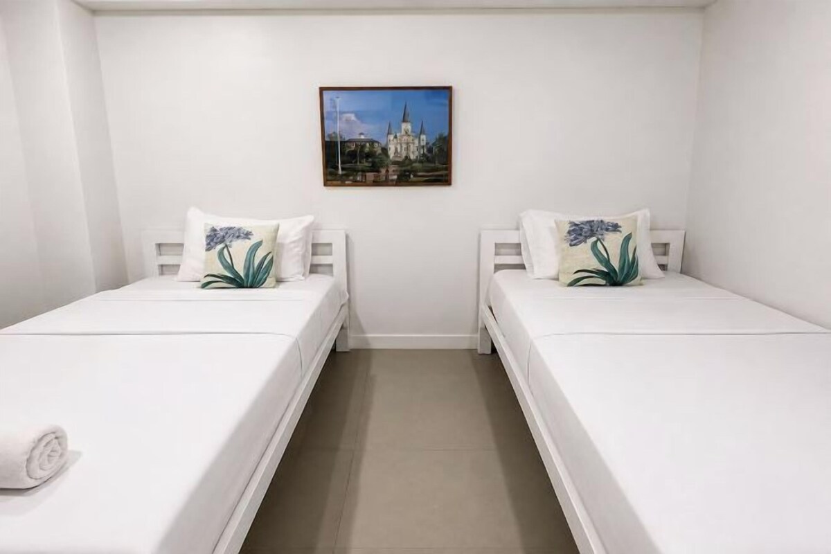 A room with two single beds, a small table, and a wall-mounted picture.
