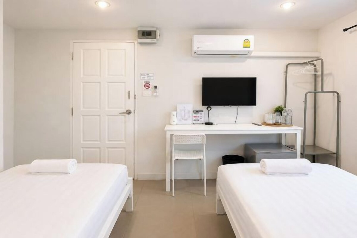 A hotel room with two beds, a desk with a computer, a TV, and a shower area.