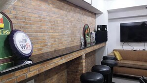 A room with a brick wall, a flat-screen TV mounted above a sofa, and a bar area with stools and a sign indicating free WiFi. - 101 Seoul Hostel (Bangkok)