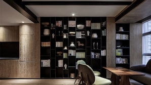 A modern living room with a wooden floor, a bookshelf filled with books and decorative items, a dining table, and a sofa. - Chongqing David‘s Deer Boutique Hotel (Chongqing)
