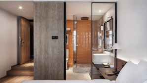 A modern hotel room with a wooden door, a glass partition, a large mirror, a bedside table, and a bed. - Chongqing David‘s Deer Boutique Hotel (Chongqing)