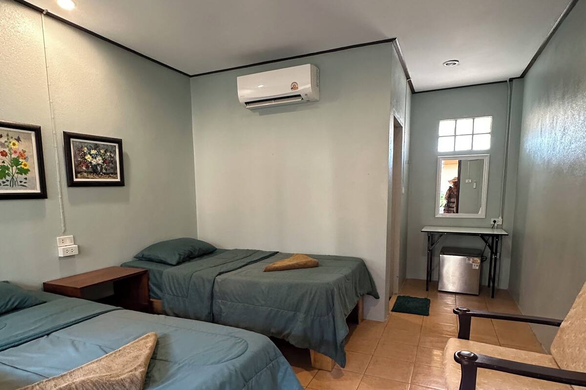 Habitación con dos camas, una silla, una mesita, aire acondicionado y ventana con vistas.