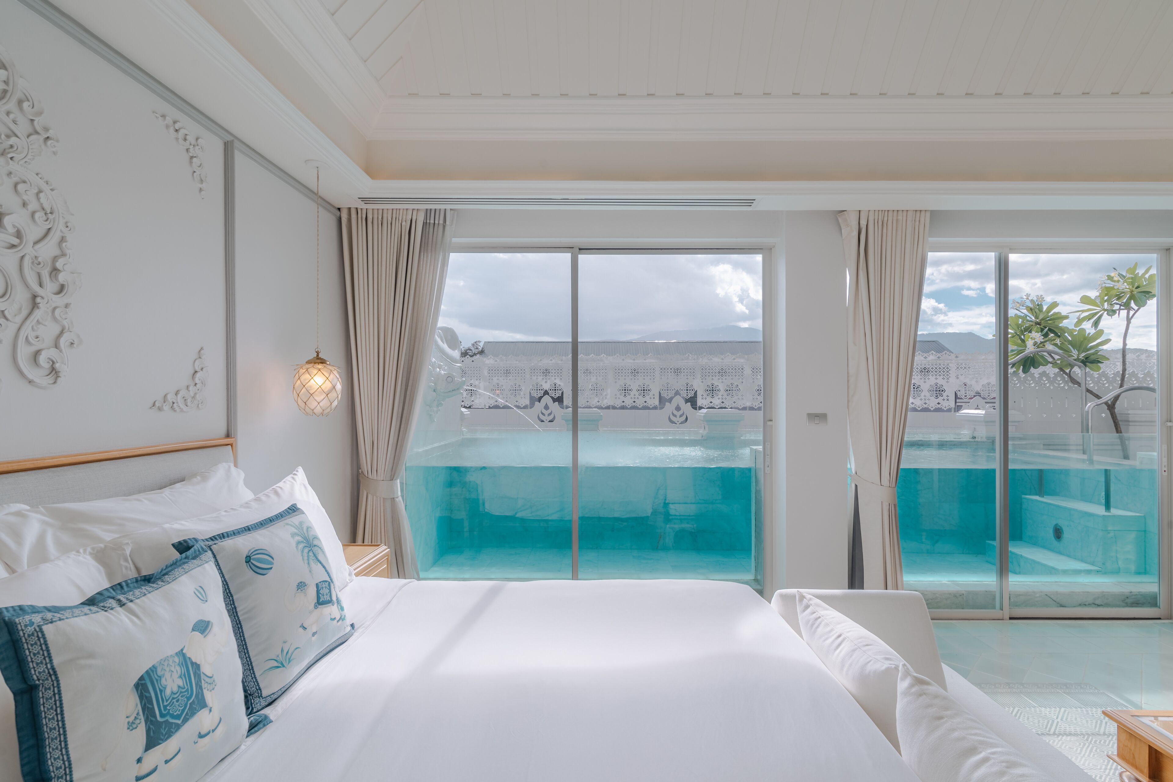 Una habitación de hotel con una cama grande, vistas a una piscina infinita y un balcón con puerta de vidrio.