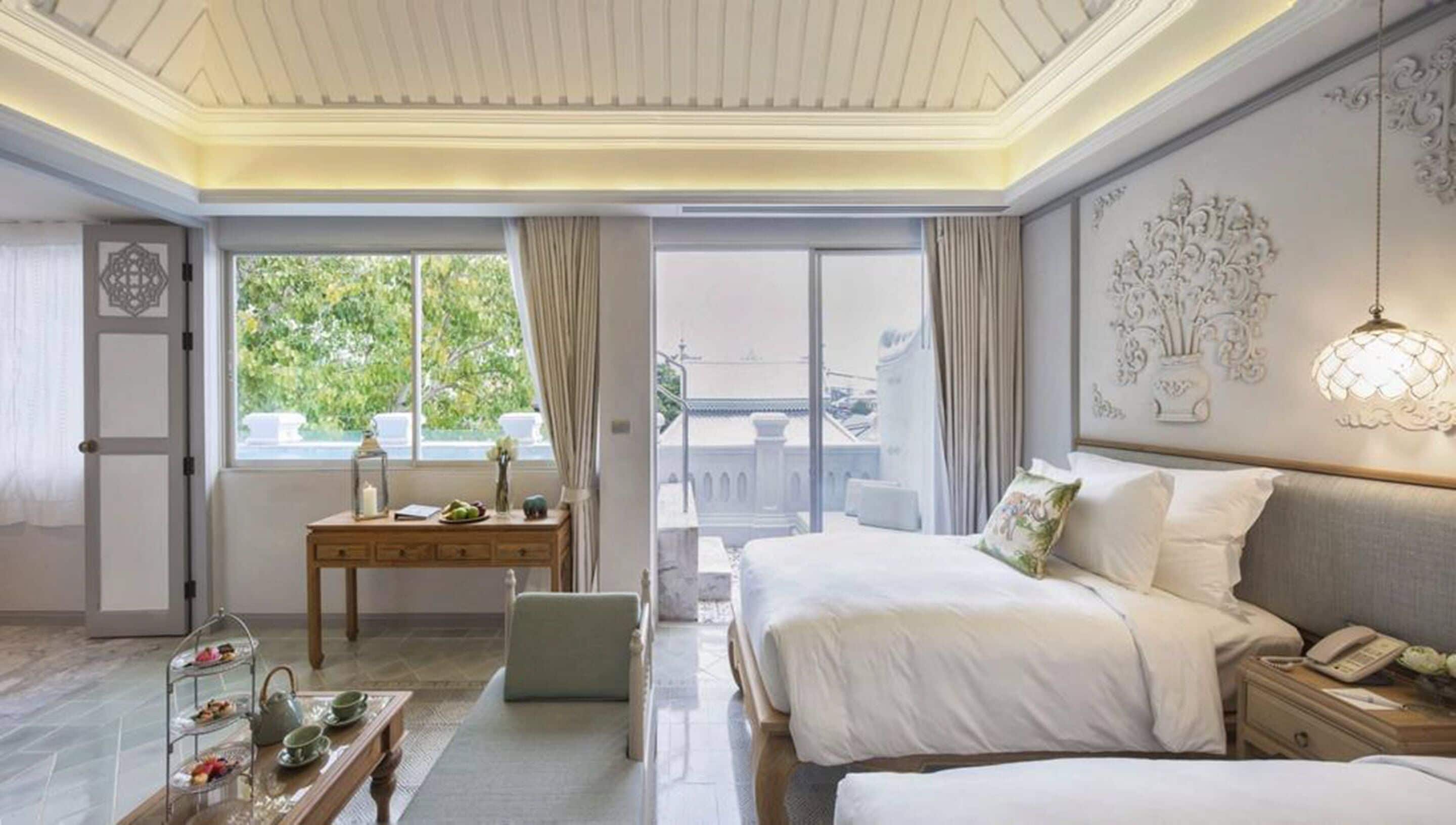 A hotel room with a large bed, a desk with a chair, a small table with a tray of food, and a view of the outdoors.