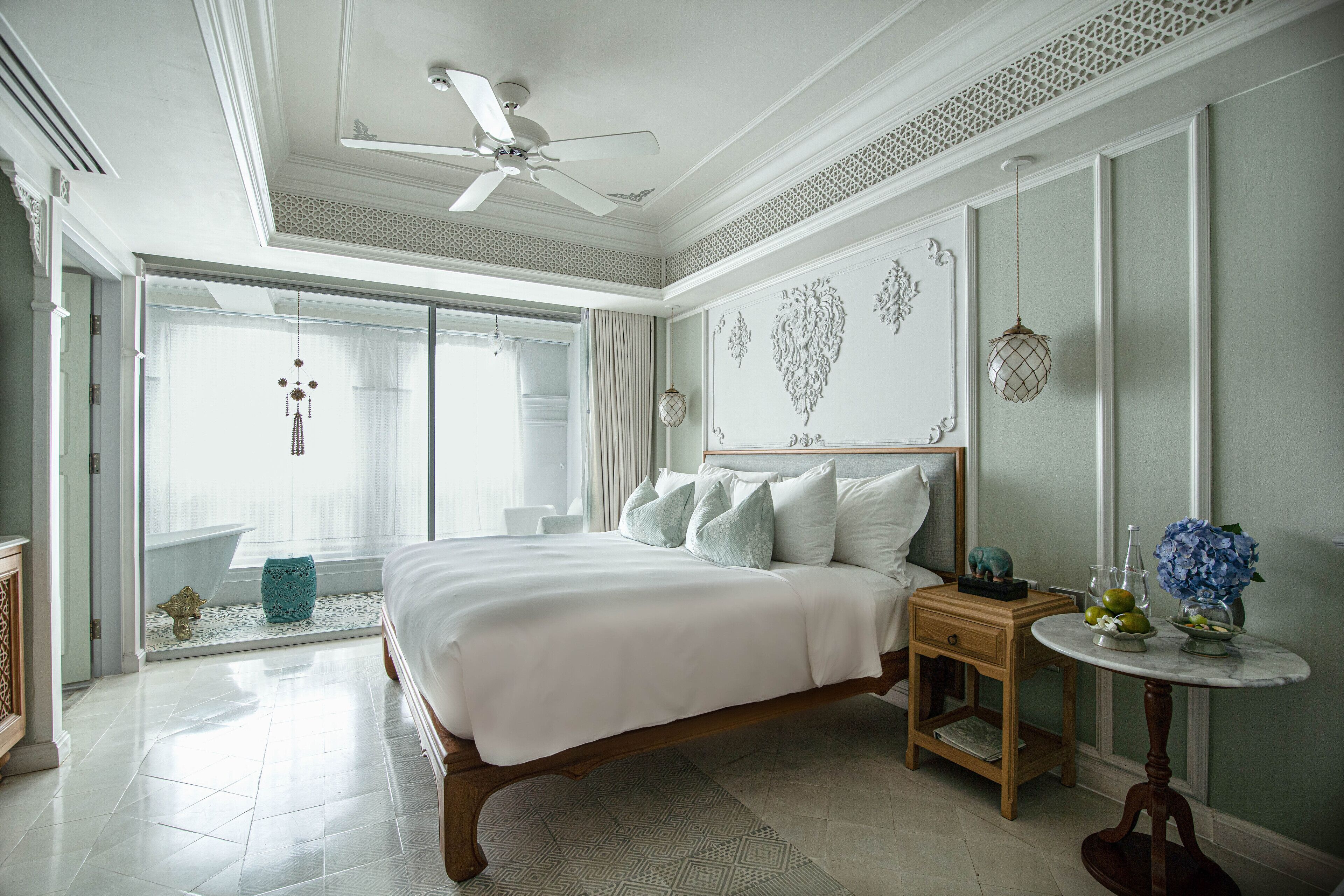 A spacious bedroom with a large bed, a ceiling fan, a nightstand, and a small table with decorative items.