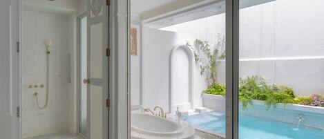 Un baño moderno con ducha a ras de suelo, bañera independiente y una pequeña zona de piscina con plantas.