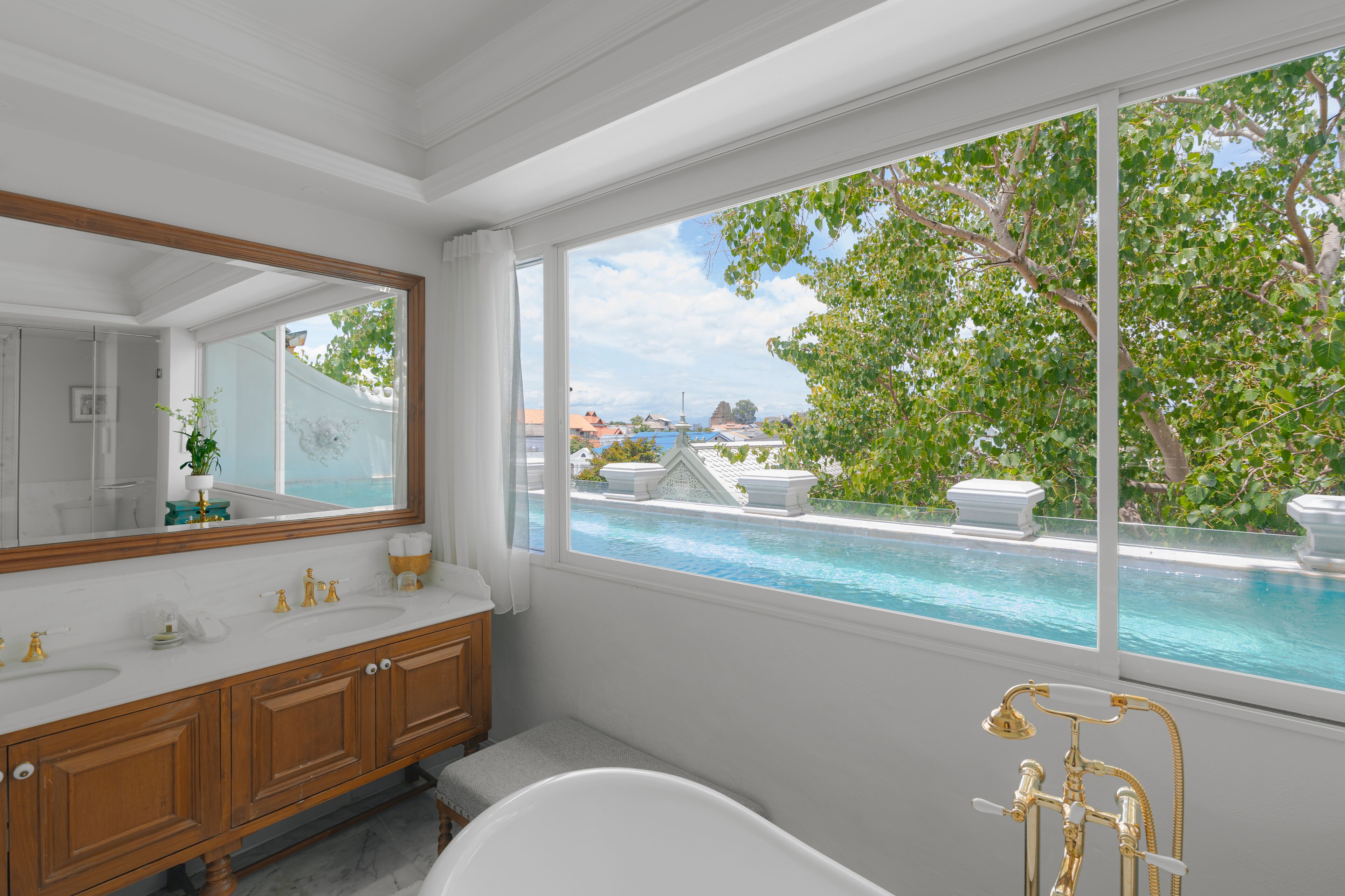 A bathroom with a large window, a bathtub, and a vanity with a mirror.