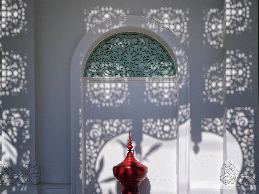 A room with a decorative window, a red object in the foreground, and intricate wall patterns.