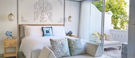 A modern bedroom with a large bed, a sofa, a glass coffee table, and a view of the outdoors.