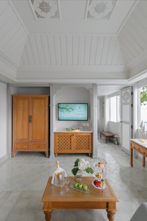 A spacious room with a wooden cabinet, a television, a dining table with fruit and glassware, and a patterned floor.