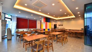 A modern dining area with wooden tables and chairs, a colorful wall, and recessed ceiling lighting.