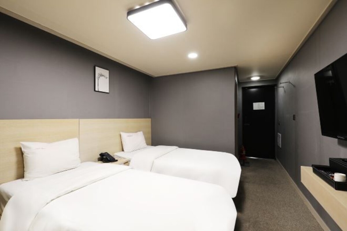 Una habitación de hotel con dos camas, un televisor de pantalla plana y un escritorio pequeño con teléfono.