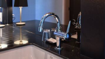 A modern bathroom with a black countertop, chrome faucet, and a white sink. There are wall-mounted lights and a mirror above the sink.